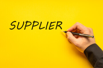 Male hand writes in black pen the word supplier on a yellow background with copy space. Business concept photo