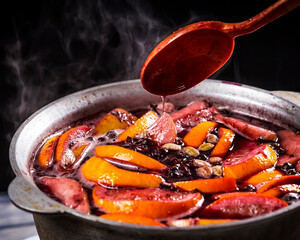 Big kettle pot of traditional hot steaming Christmas drink mulled red spiced wine boiling with...