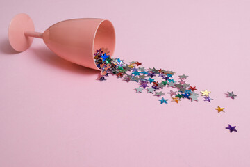 It's spilled drink of colorful stars from a pink glass on a pastel pink background. Minimal party concept.