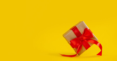 Gift box in craft paper with red ribbon bow on yellow color backdrop.
