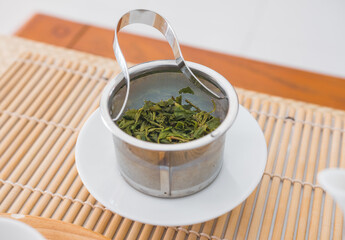 Huang Shan Mao Feng, fresh green tea leaves, spring harvest. From Anhui mountain in China. Close up of wet leaves in a teapot metal filter on a white porcelain plate.