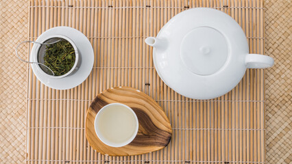 Tea set top view. Porcelain teapot, teacup and green tea in a metal filter on a bambou tray. Beautiful professional shot of the teaware. Morning breakfast.