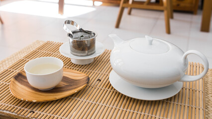 Tea set. Porcelain teapot and teacup, fresh organic green tea leaves in a metal filter. Beautiful professional shot of the teaware. Morning breakfast and caffeine.