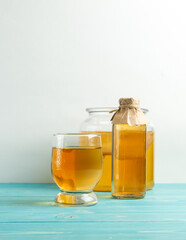 Homemade Kombucha lemonade in a glass, a bottle with a drink and a jar with a mushroom on a light background