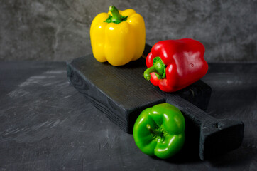 Composition with red, yellow and green bell pepper paprika on a grey background.