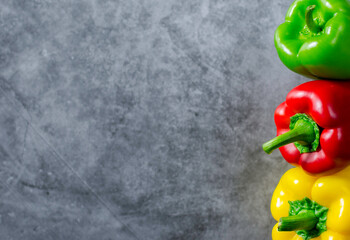 Red, yellow and green bell pepper paprika on a grey background. Stacked in vertical position.