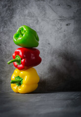 Red, yellow and green bell pepper paprika on a grey background. Stacked in vertical position.