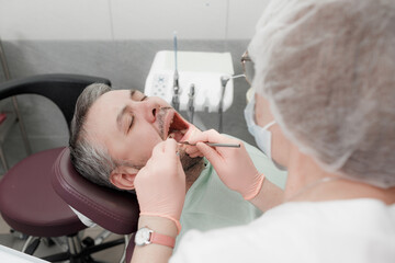 A female dentist treats the teeth of a male patient in the office of a dental clinic.His mouth wide open. Concept of medicine, dentistry and healthcare. Dental equipment
