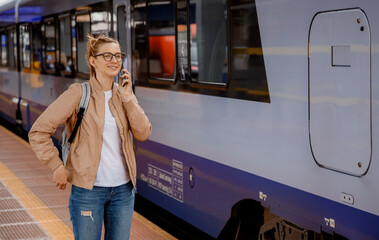 Woman with glasses on the platform near the train. Girl with a cell phone at the train station near the blue train. Travel by rail. Bydgoszcz.