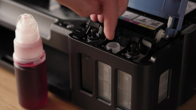 Video instruction, technology, media, office, stationery concept - close-up of male hands preparing new inkjet printer for launch. step 10: insert nozzle of bottle into inlet stand upside down pur ink