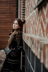 Young attractive woman in trench coat thoughtfully looking in camera while walking around cozy city street