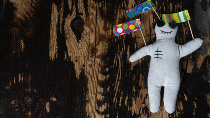 Close-up of a voodoo doll with straight pins and strange flags on dark wooden background. Mystic concept.