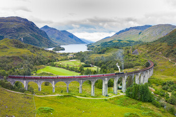 Classic Steam Train travelling across an old bridge with dramatic landscape in the background in Scotland 