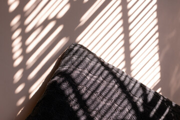 Knitted pillow with blind shadows on the wall. Knitted pillow with jalousie shadows. Winter cozy accessories.