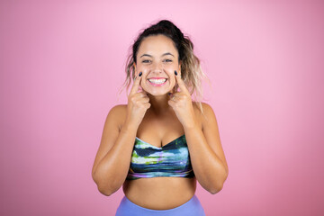 Young beautiful woman wearing sportswear over isolated pink background smiling confident showing and pointing with fingers teeth and mouth