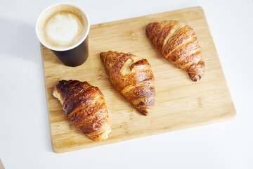 Golden fresh croissants with coffee on a wooden tray close up