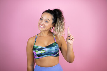 Fototapeta na wymiar Young beautiful woman wearing sportswear over isolated pink background showing and pointing up with fingers number one while smiling confident and happy
