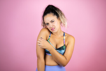 Young beautiful woman wearing sportswear over isolated pink background with pain on her shoulder and a painful expression