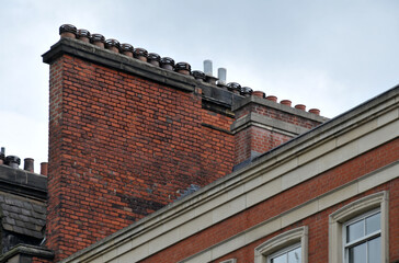 A large row of old fashioned traditional clay chimney pots on a red brick support against a grey sky from when buildings where built with coal burning heating