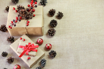 Natural Christmas background with gifts, pine cones, red decorations and a jute fabric