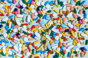 Creative layout of colorful pills and capsules on blue background with summer sun and sharp shadow. Minimal medical concept. Pharmaceutical, Covid-19 or Coronavirus. Flat lay, top view.