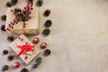 Natural Christmas background with gifts, pine cones, red decorations and a jute fabric