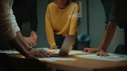 Close Up of Diverse Multiethnic Team Having Conversation in Meeting Room in a Creative Office. Colleagues Lean On a Conference Table, Look at Laptop Computer and Make Notes with Pencils on Notebooks.