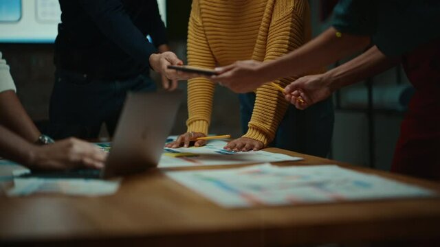 Close Up of Diverse Multiethnic Team Having Conversation in Meeting Room in a Creative Office. Colleagues Lean On a Conference Table, Look at Laptop Computer and Make Notes with Pencils on Notebooks.