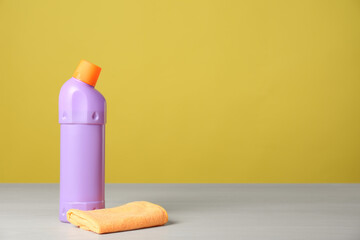 Bottle of cleaning product and microfiber cloth on light table. Space for text