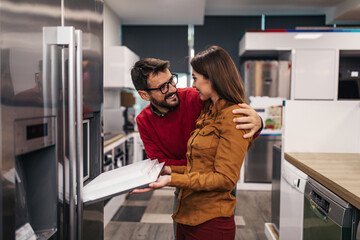 Young couple, satisfied customers choosing fridges in appliances store.