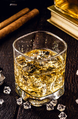 square glass with whiskey and ice, high quality distilled beverage, cigar and lighter in the background. Image of pub, bar, restaurant or cellar