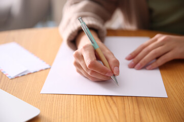 Woman writing letter at wooden table, closeup