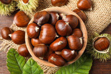 Fresh sweet edible chestnuts on brown wooden table, flat lay