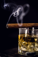 detail of cigar with glass of whiskey giving off smoke on black background.Picture of pub, bar or restaurant