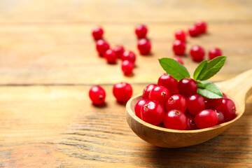 Spoon with tasty cranberries and green leaves on wooden table, closeup. Space for text