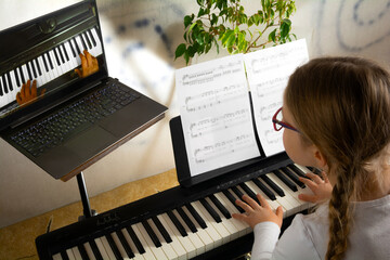 Girl learning to play the piano in distance learning via laptop over the Internet