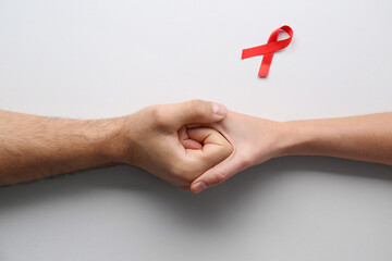 People holding hands near red awareness ribbon on white background, top view. World AIDS disease day