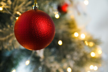 Beautiful red holiday bauble hanging on Christmas tree against blurred fairy lights, closeup. Space for text