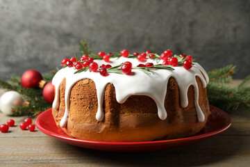 Traditional Christmas cake decorated with glaze, pomegranate seeds, cranberries and rosemary on wooden table