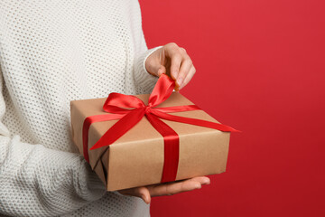 Woman holding Christmas gift box on red background, closeup