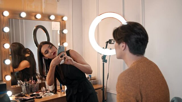 Makeup studio - woman artist taking photos on her phone of her male model with makeup on