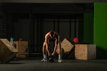 Fototapeta na wymiar Full-length photo of a handsome man with a naked torso exercising with a kettlebell on a dark background