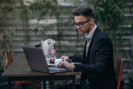 Young successful businessman working on a laptop while sitting in coffee bar during work break lunch. Speaking on his phone while working and drinking coffee.