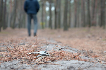 Young man loses his keys bunch on Russian autumn fir wood path. Carelessness and losing keys concept