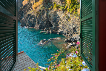 View from an open window over a small bay with swimmers sitting on the rocks, near the village of Vernazza, Italy, part of the Cinque Terre