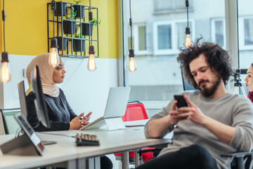 Bearded employee guy with afro haircut talking on his phone while being surrounded by his multiethnic coworkers. Businessman working in a casual startup modern environment.