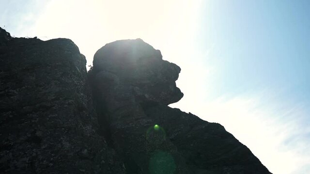 A handheld shot of an enormous cliff in the shape of a human face just from one perspective of looking, located near the sea coast.
