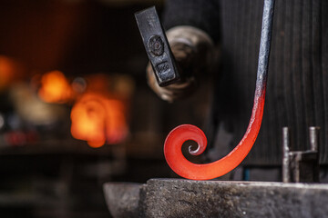 Close-up of the hands of a blacksmith twisting a spiral with a hammer, putting a red-hot iron blank...