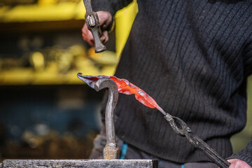 A close-up of the hands of a blacksmith forging a thin iron sheet in the shape of a plant by...