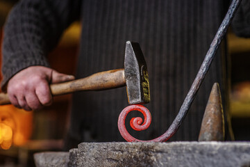 The blacksmith hits the red-hot workpiece in the forge with a hammer and glowing sparks fly in all...